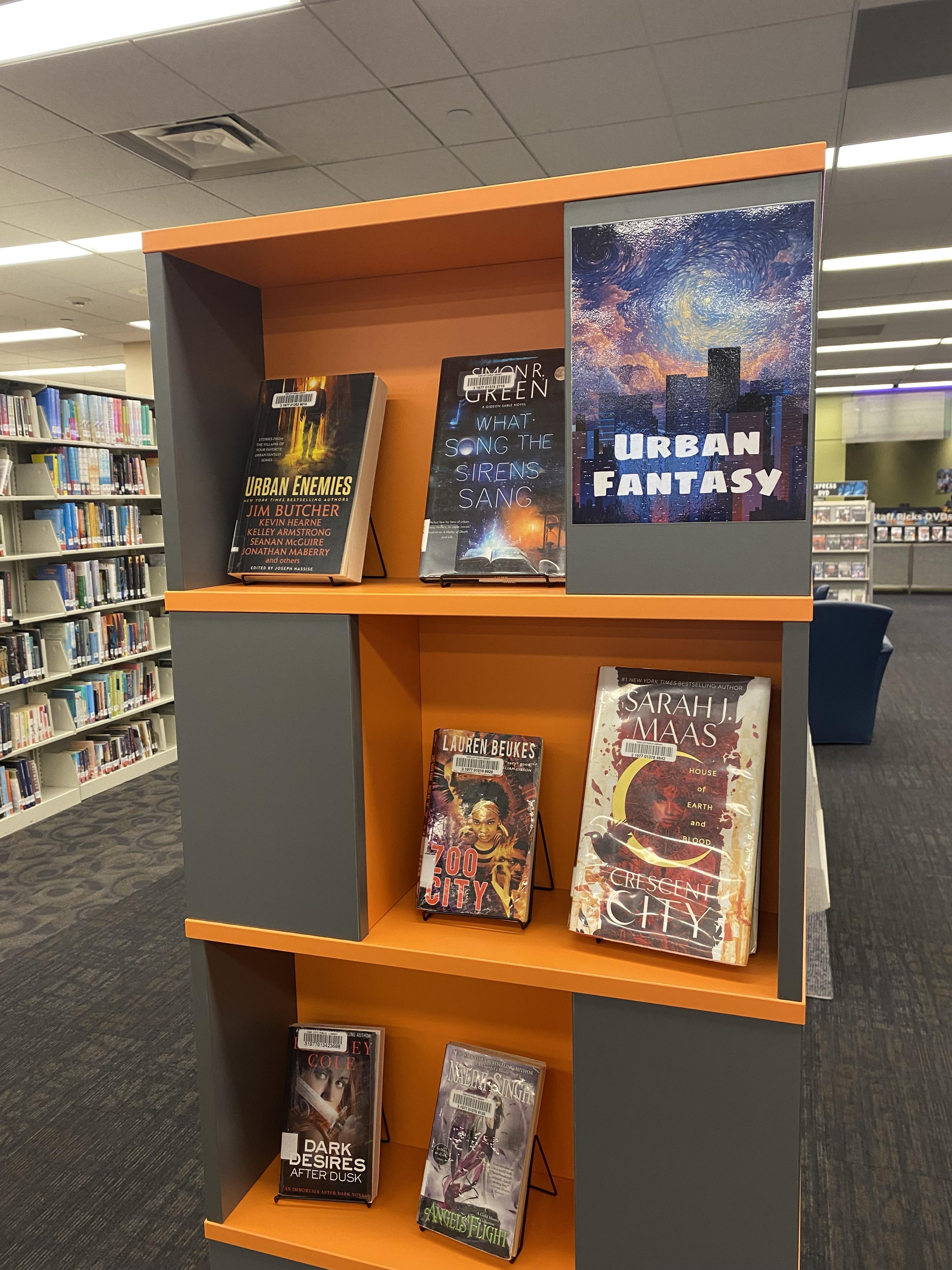 Shelf on Urban Fantasy book display includes titles by Simon R. Green, Lauren Beukes, Sarah J. Maas, Kresley Cole, and Nalini Singh. 